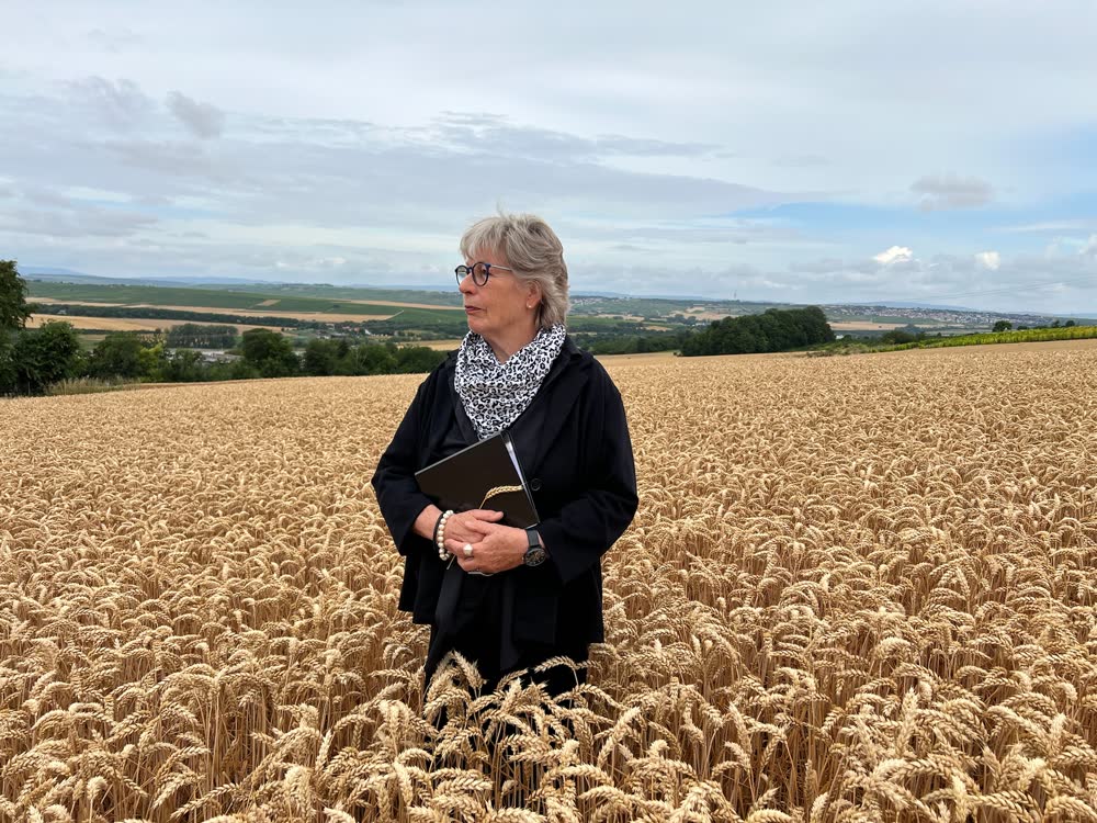 Trauerrednerin Beate Berdel-Mantz steht mit einer Redemappe in einem sommerlichen Kornfeld bei Sörgenloch in Rheinhessen.